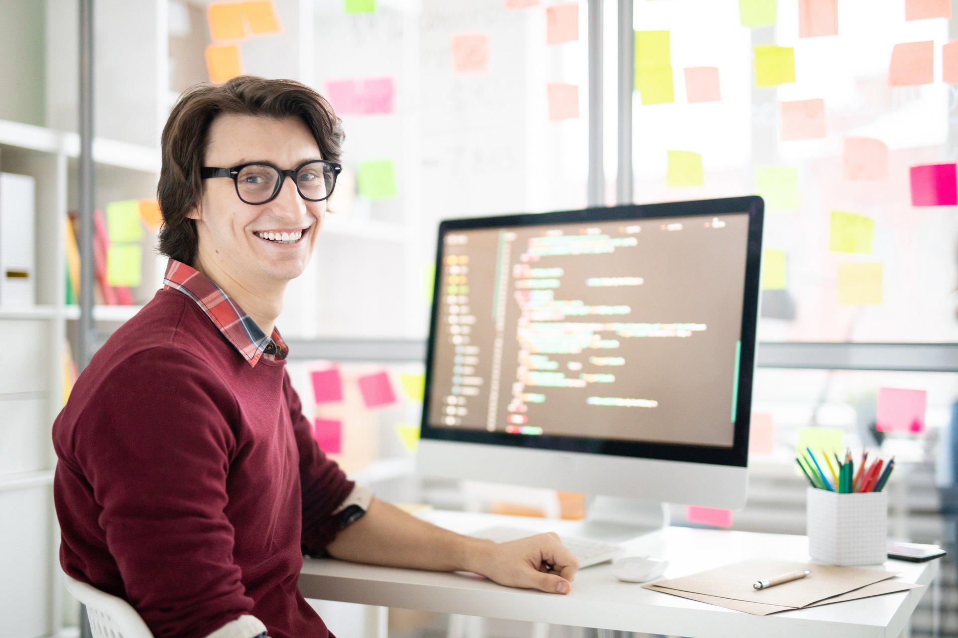 ein junger Mann mit Brille sitzt an einem Schreibtisch und arbeitet an einem Computer