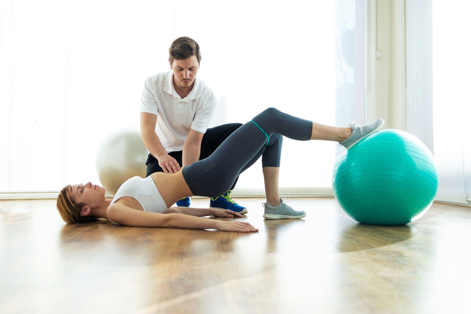 ein Physiotherapeut mit einer Frau bei einer Übung mit dem Gymnastikball