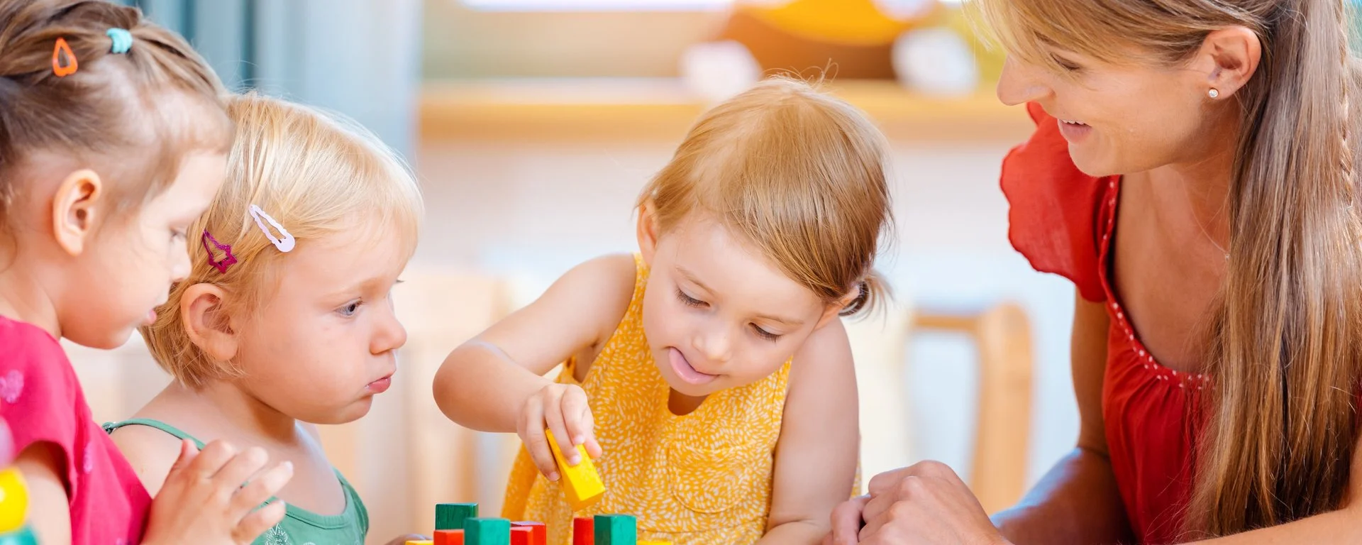 eine Erzieherin spielt mit Bauklötzen mit einer Kindergruppe