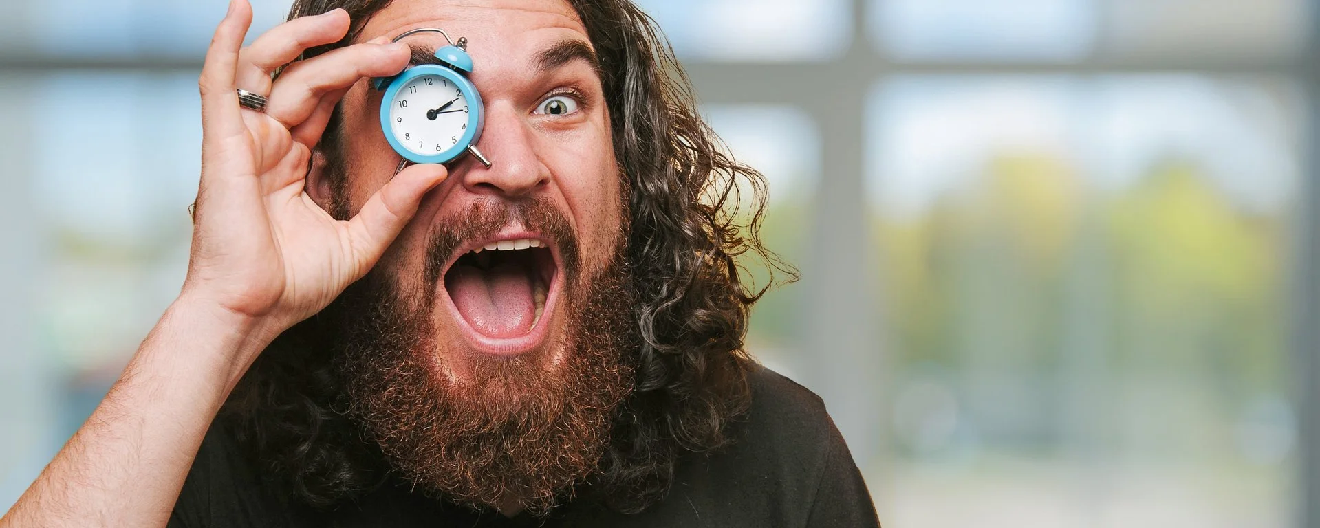 ein Mann hält sich einen kleinen Wecker vor ein Auge