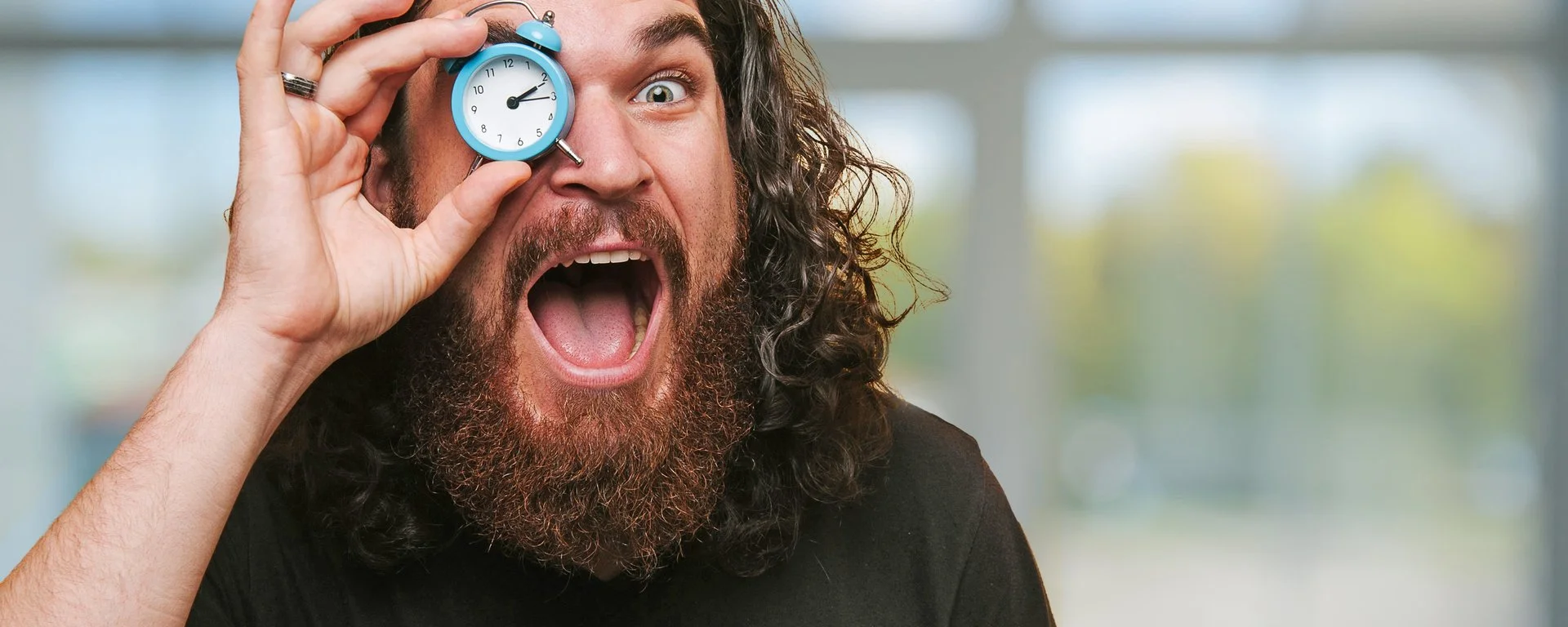 ein Mann hält sich einen kleinen Wecker vor ein Auge