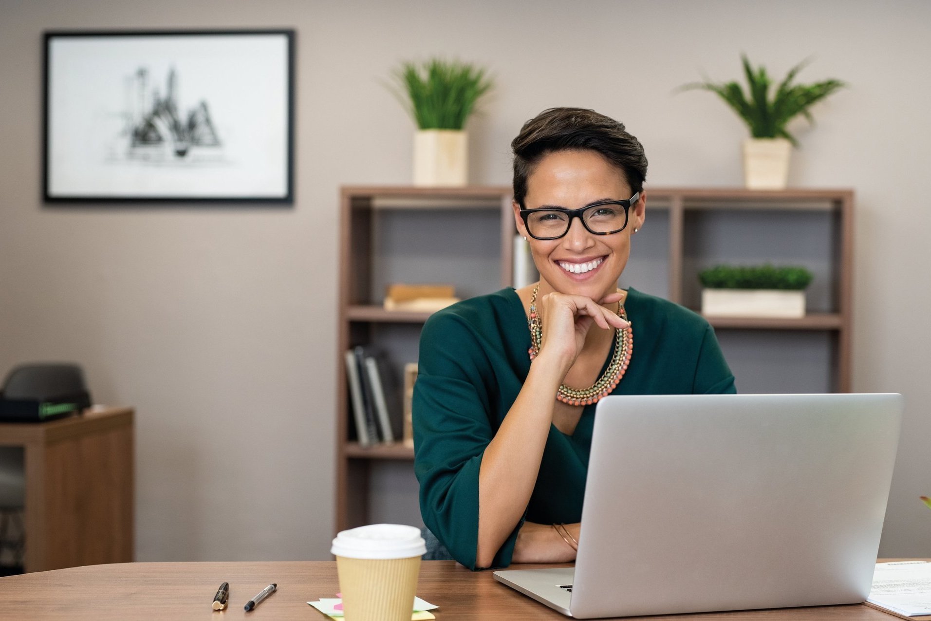 eine lächelnde Dame mit Brille arbeitet an einem Laptop