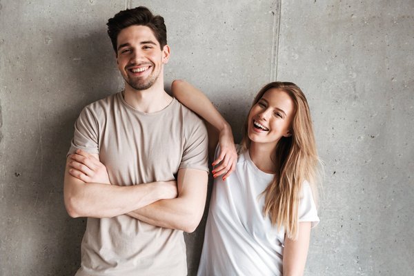 ein junger Mann und eine junge Frau stehen lächelnd vor einer grauen Wand