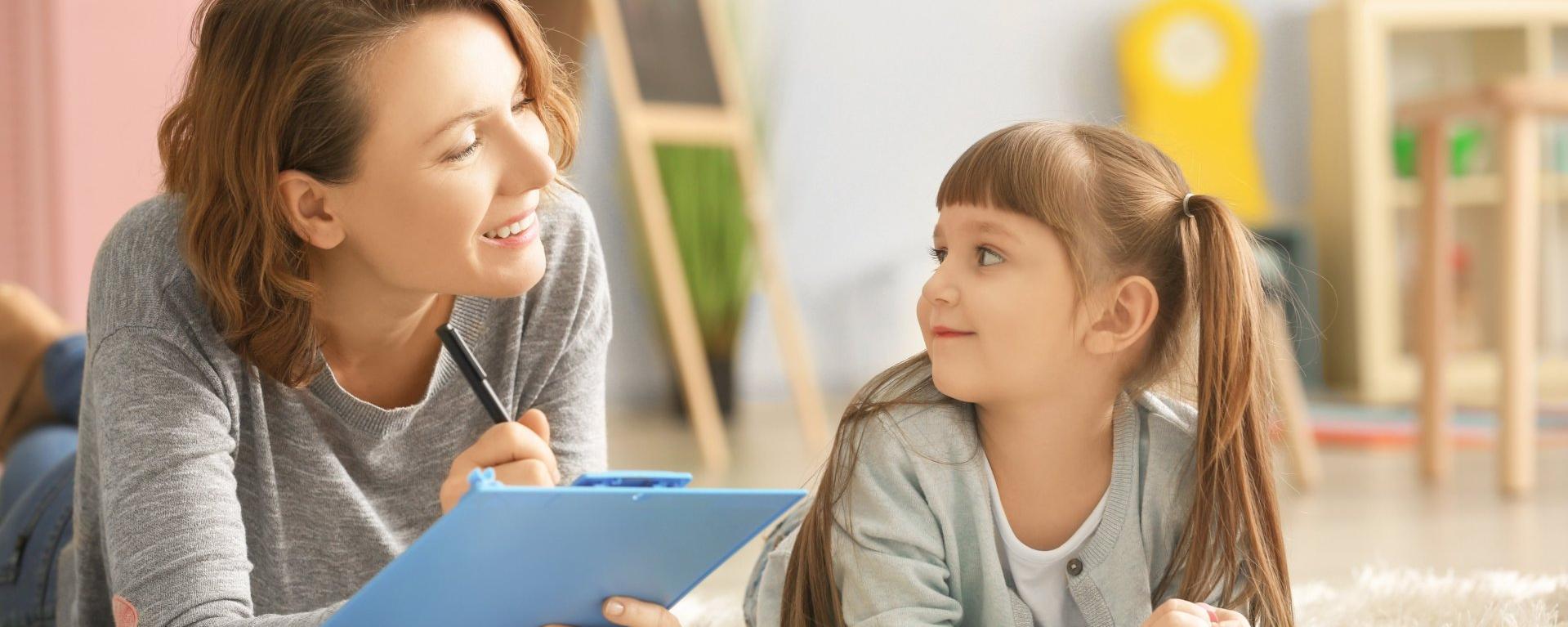 eine Logopädin und ein Mädchen auf einem Teppich bei einer Sprechübung