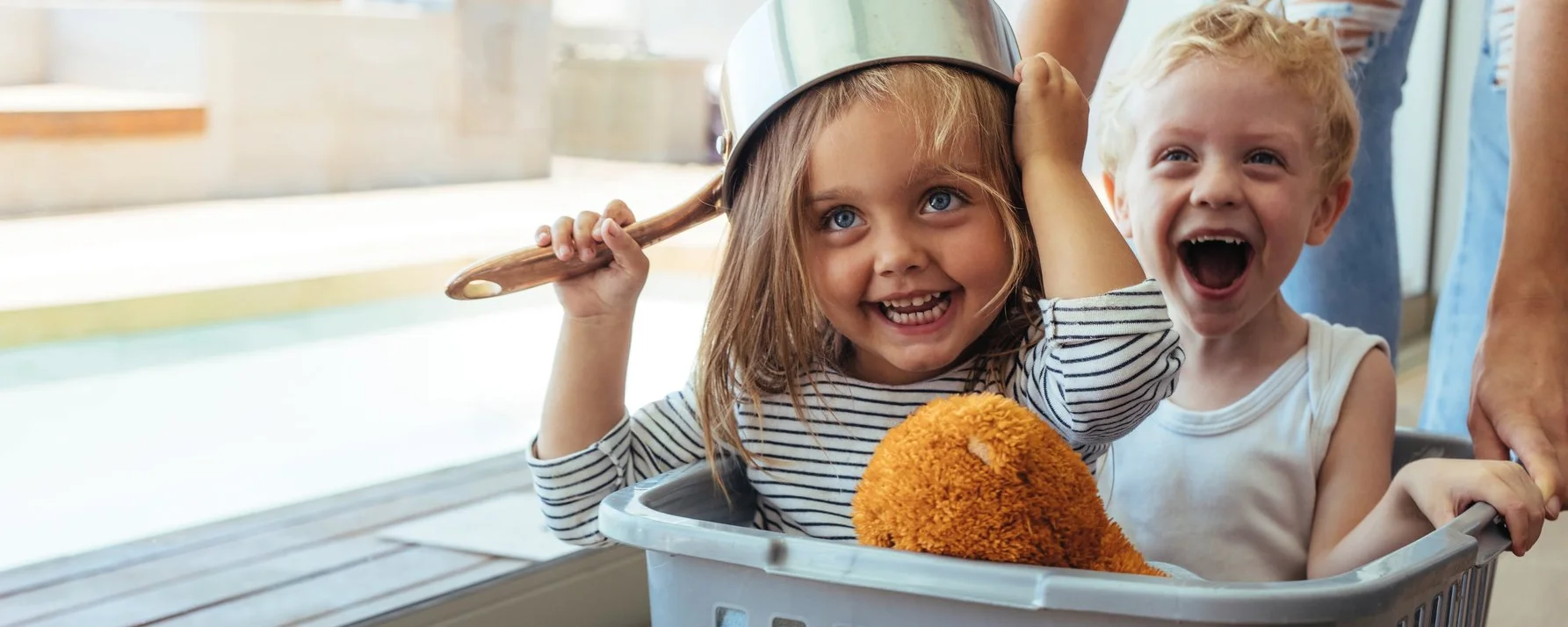 Zwei Kinder sitzen lachend in einem Wäschekorb