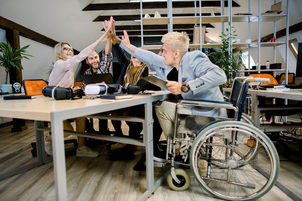 mehrere junge Menschen geben sich 'high five'. Ein junger Mann der Gruppe sitzt im Rollstuhl