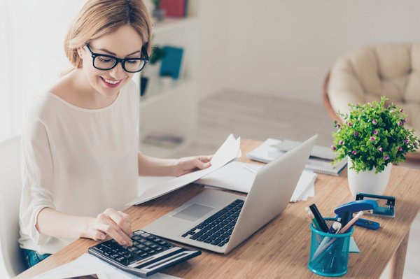 eine Frau arbeitet an ihrem Laptop und berechnet etwas mit ihrem Taschenrechner