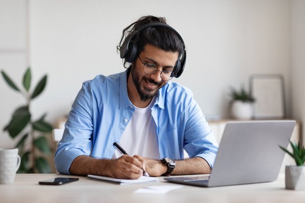 ein jüngerer Mann mit Brille nimmt an seinem Laptop bei Live-Unterricht teil und macht sich Notizen