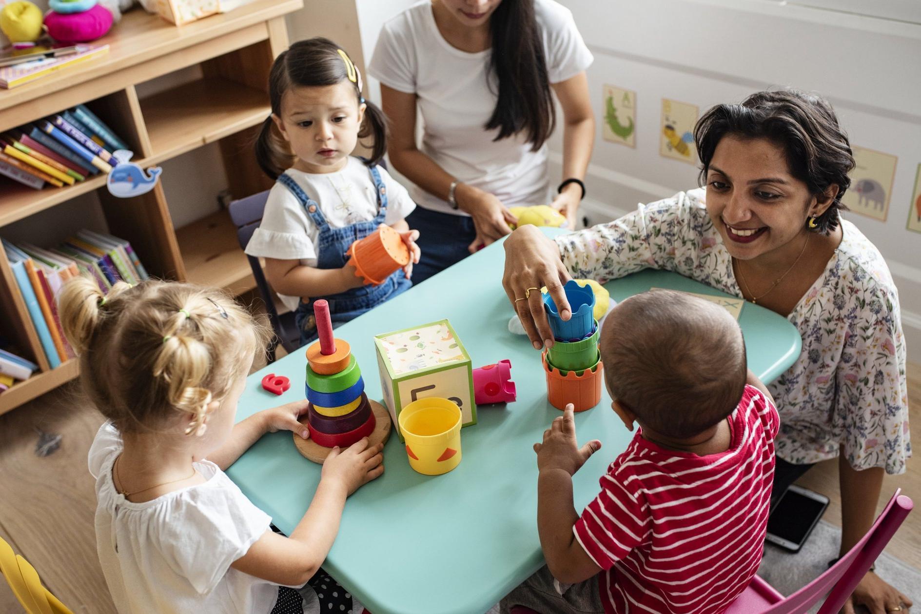 eine pädagogische Mitarbeiterin baut gemeinsam mit Kindergartenkindern Türme
